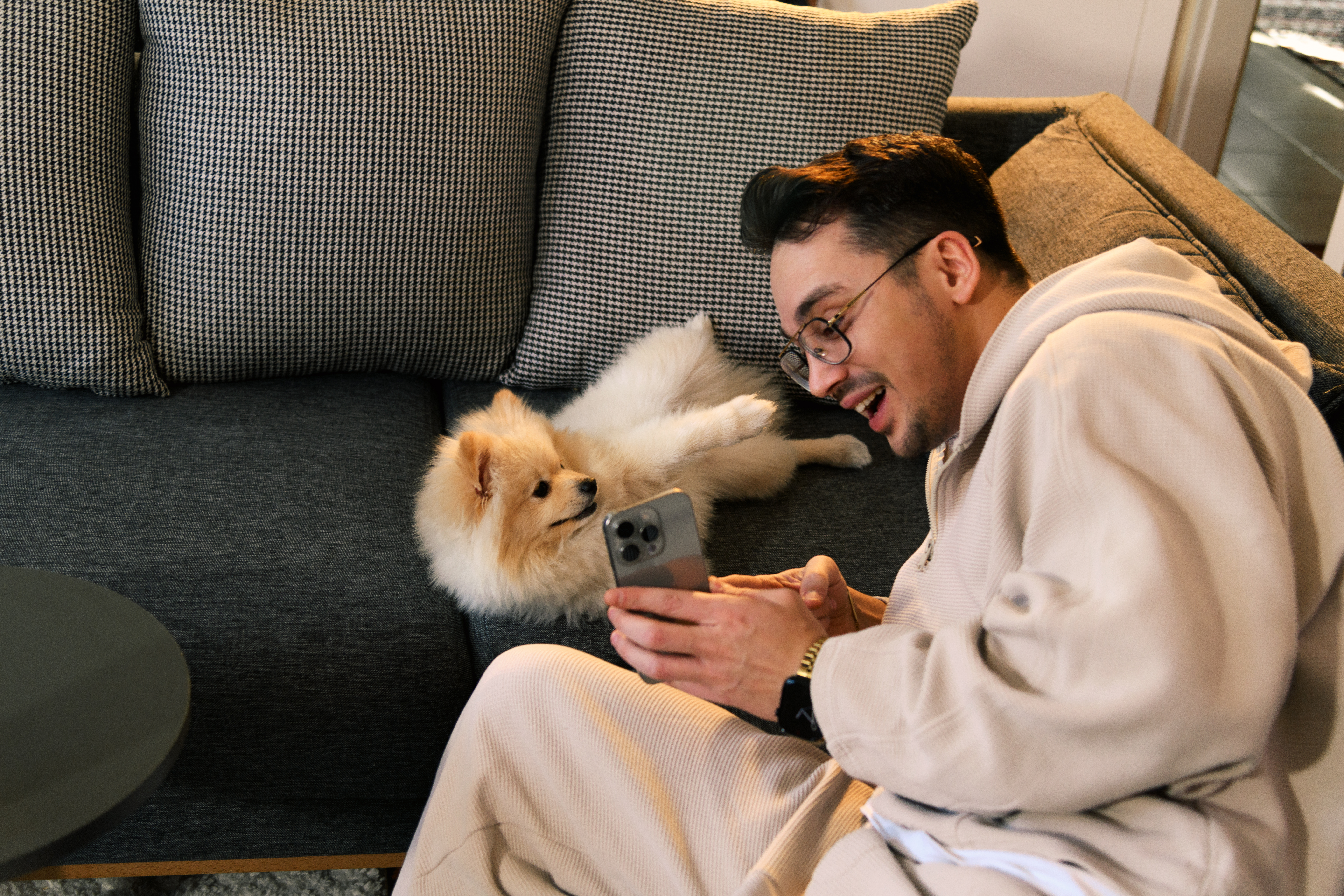 A woman relaxing on a sofa with her dog while using a smartphone